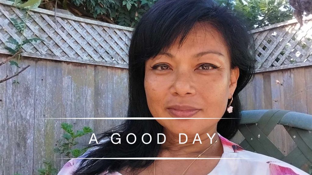 Portrait of Genevieve Cheung outdoors in soft daylight with the words “A Good Day” overlaid, expressing calm presence, simplicity, and quiet contentment.