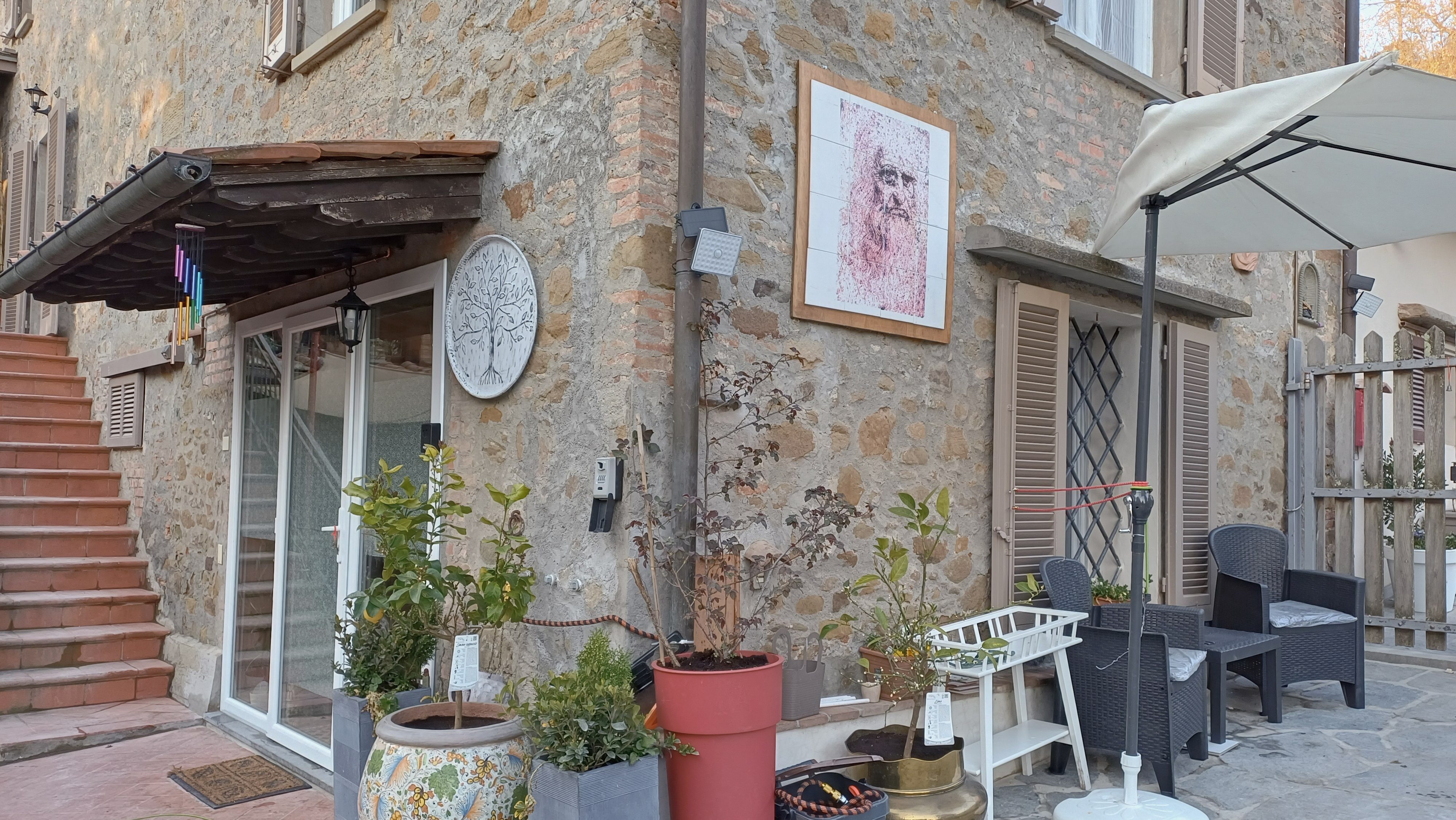 SStone house entrance at Genevieve Grove in Vinci, Tuscany, showing traditional architecture, plants, and the portrait of Leonardo da Vinci on the exterior wall.